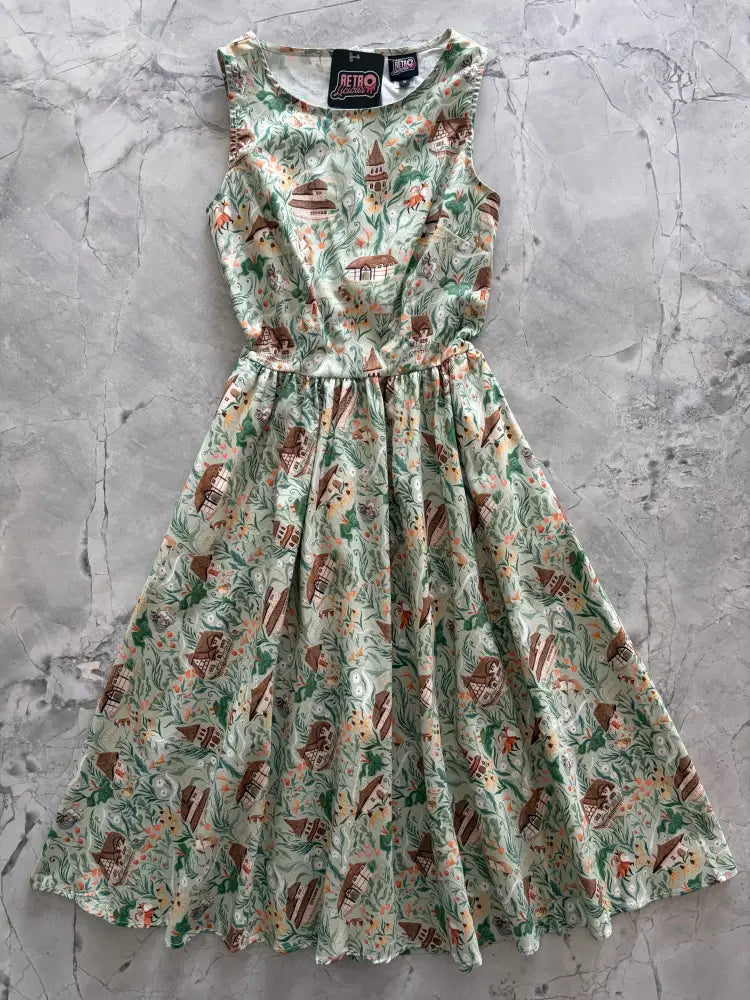A sleeveless light green cotton midi dress with brown house and foliage print titled Cottage Tales Green Fox Print