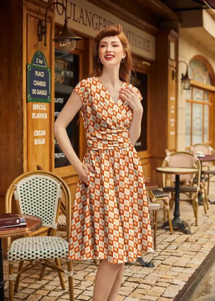 A woman wears a vintage-style cotton dress with an orange and cream checkered pattern and a flared skirt