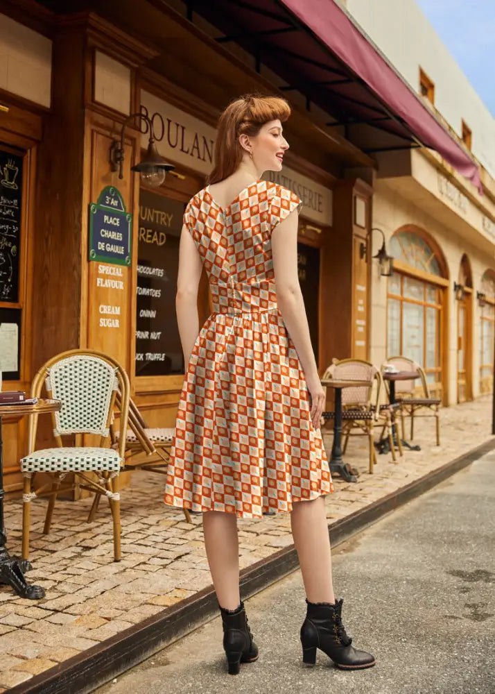 A woman wears a cotton candy greta vintage cotton dress with an orange and cream checkered pattern and knee-length design