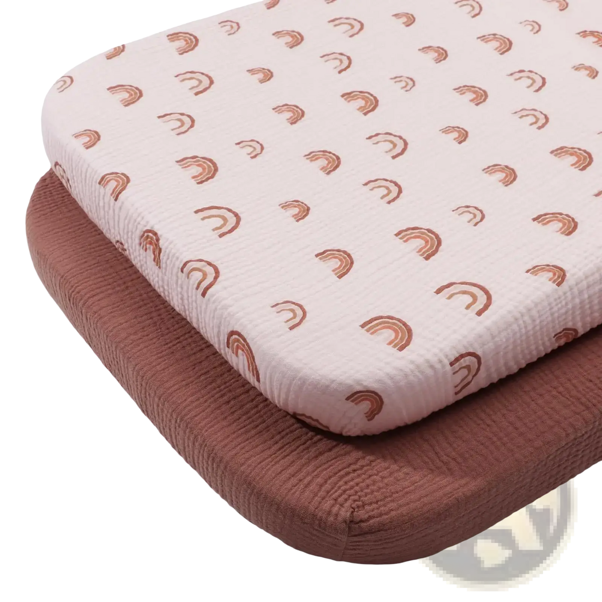 A soft pale pink cotton muslin crib sheet set featuring a textured fabric with a small brown rainbow pattern