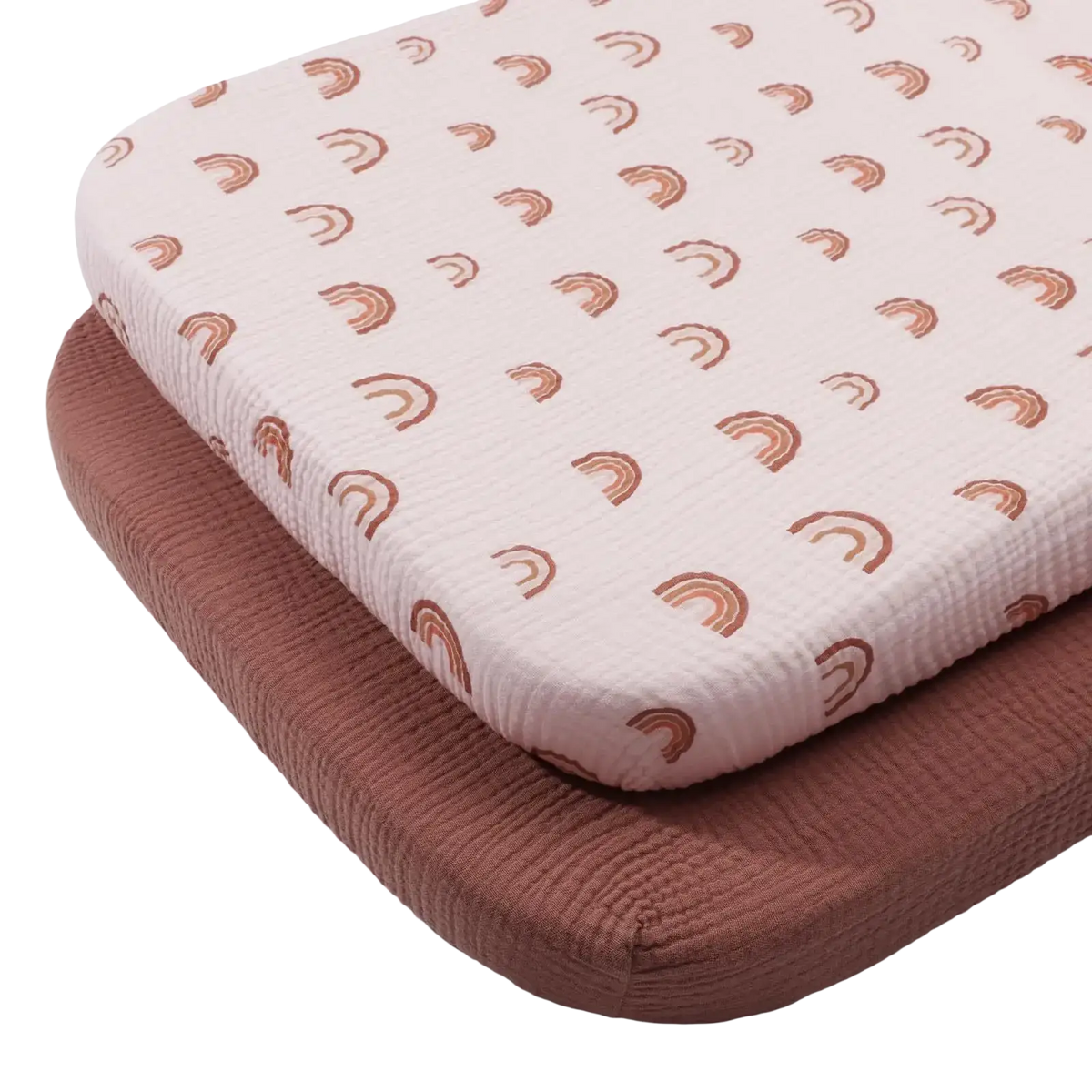 A soft pale pink cotton muslin crib sheet set featuring a textured fabric with a small brown rainbow pattern