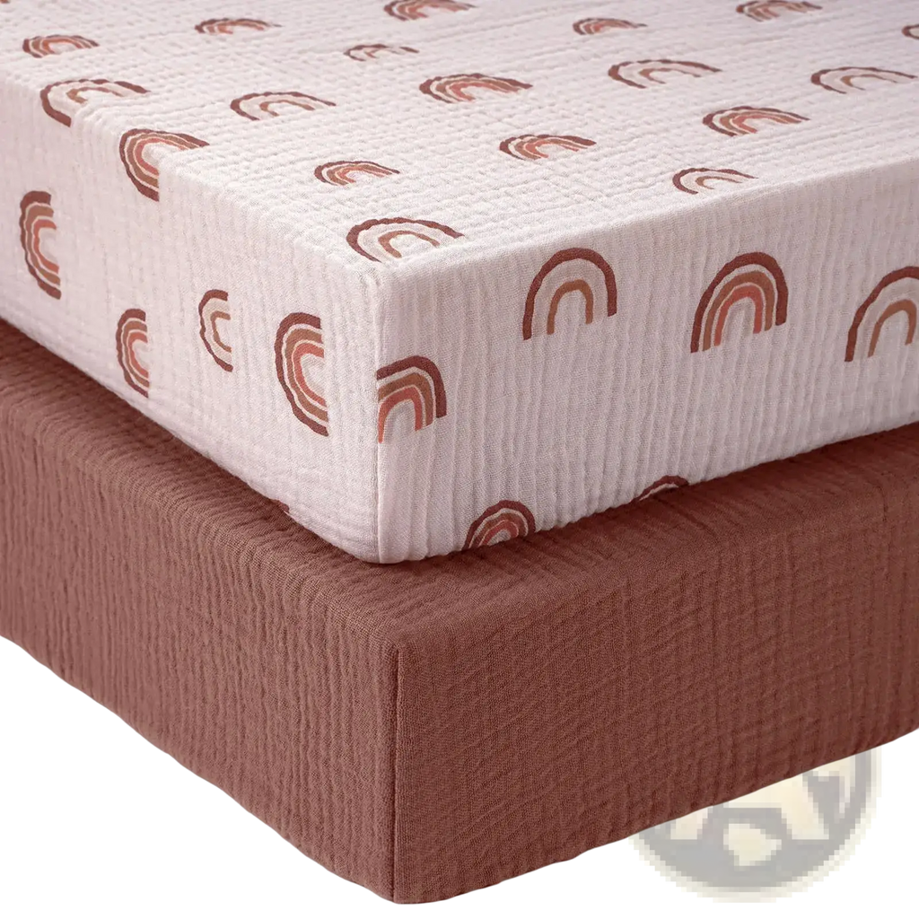 Cotton muslin crib sheet set featuring a soft off-white fabric with earthy-toned rainbow patterns for nursery use