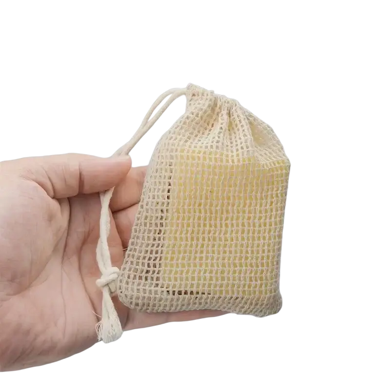 Beige cotton mesh soap saver bag with drawstring closure holding a yellow bar of soap in a 3 pack set