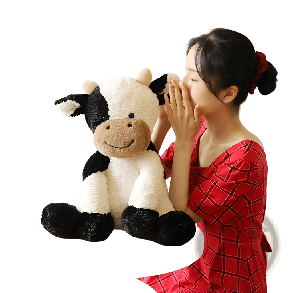 A plush black and white cow with tan snout soft stuffed animal sitting on a wooden table for decoration or play