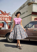 A woman wears a pink sleeveless blouse with a bow and a gray cotton cowgirl boots print Doris retro pleated skirt with pockets