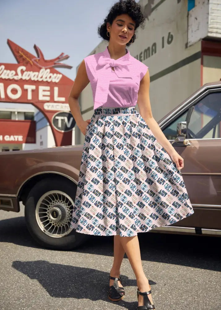 A woman wears a pink sleeveless blouse and cowgirl boots print doris retro pleated cotton skirt with pockets