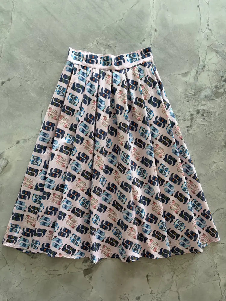 A pink retro pleated cotton skirt with pockets featuring a repeating pattern of dark blue and beige elephant silhouettes