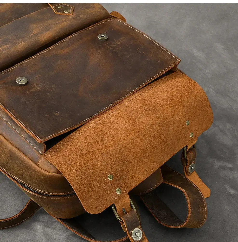 A rugged brown vintage crazy horse leather adventure backpack with suede flap and brass hardware