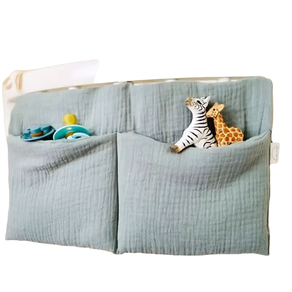 Light blue muslin crib storage bag diaper organizer with two pockets holding pacifiers and stuffed animal toys
