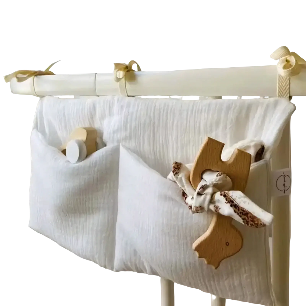 White cotton muslin crib storage bag diaper organizer with two pockets holding wooden toys and patterned fabric
