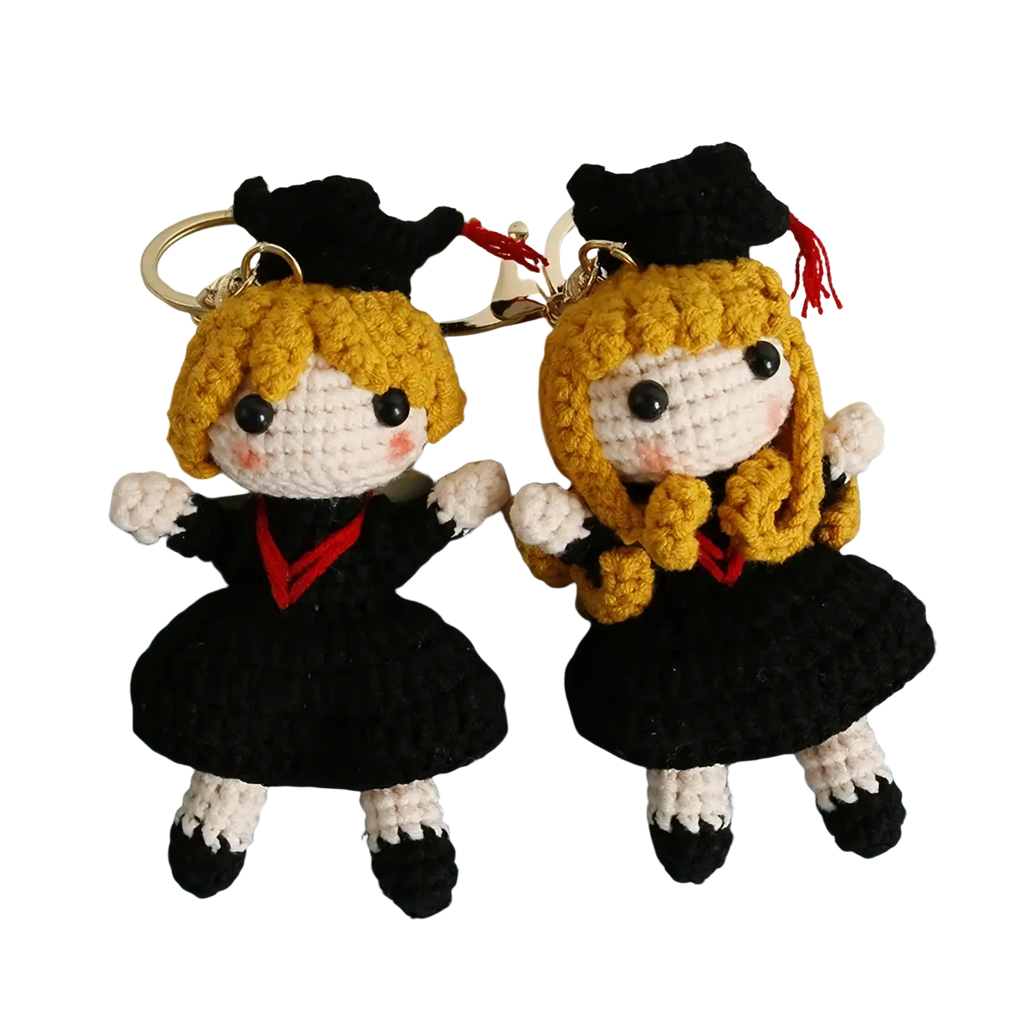 Two crocheted graduation doll keychains featuring blonde figures in black caps gowns with red accents white gloves and shoes