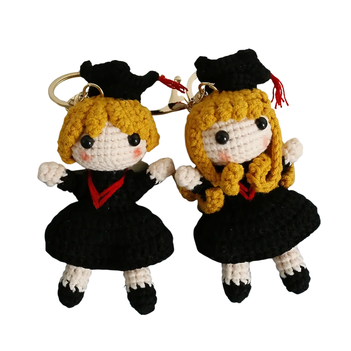 Two crocheted graduation doll keychains featuring blonde figures in black caps gowns with red accents white gloves and shoes