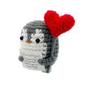 A charming gray and white crocheted positive penguin keychain with a red heart holding a positive penguin sign