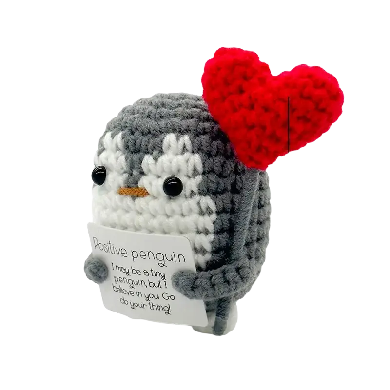A charming gray and white crocheted positive penguin keychain with a red heart holding a positive penguin sign
