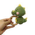 Crocheted unicorn baby comforter security blanket featuring a green crocheted dinosaur rattle with yellow spikes and pink nose attached to a wooden ring