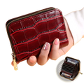 A glossy burgundy crocodile leather accordion card holder wallet with a gold zipper and pull tab