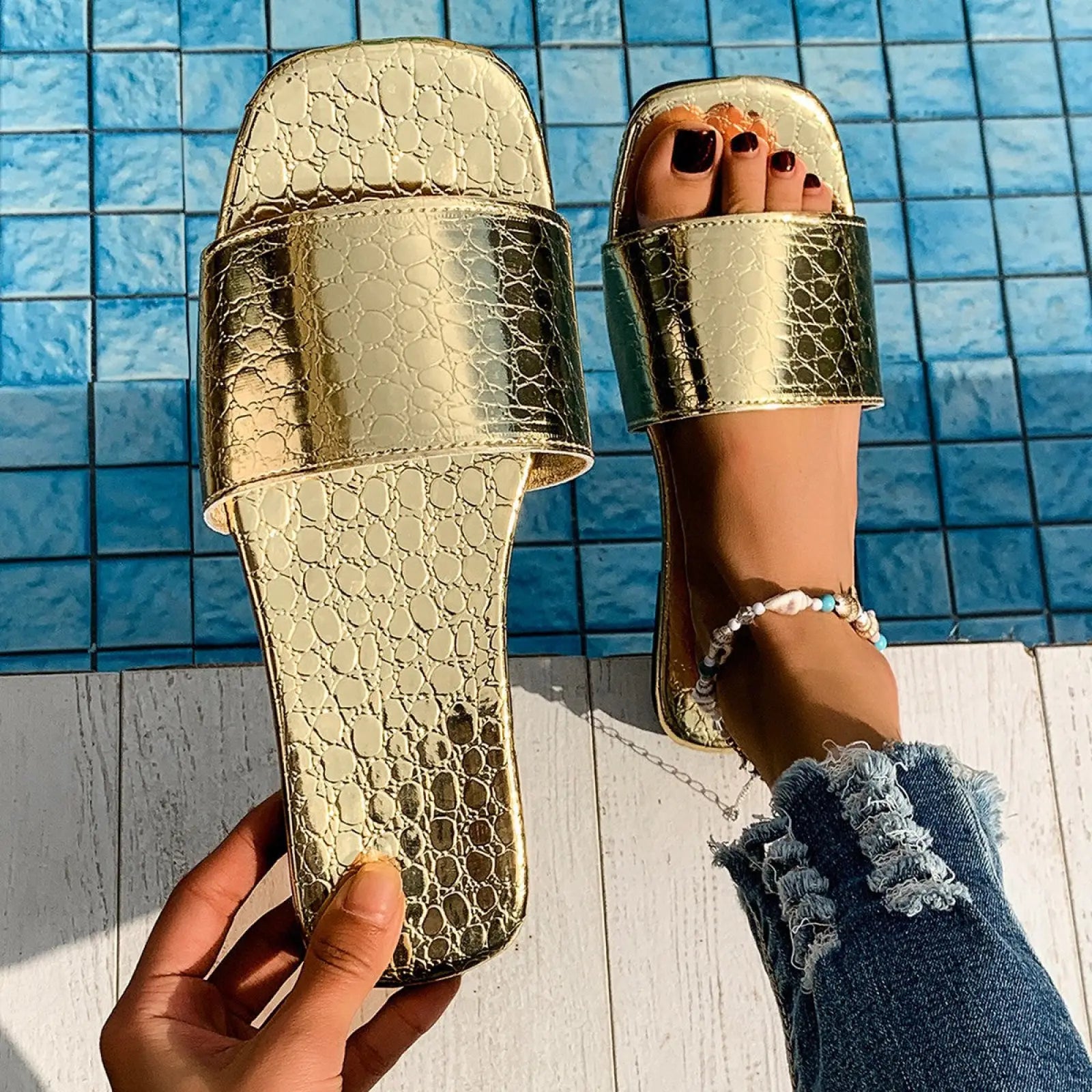 Gold-colored crocodile textured slide sandals with shiny metallic finish and square toe flat design for beach use
