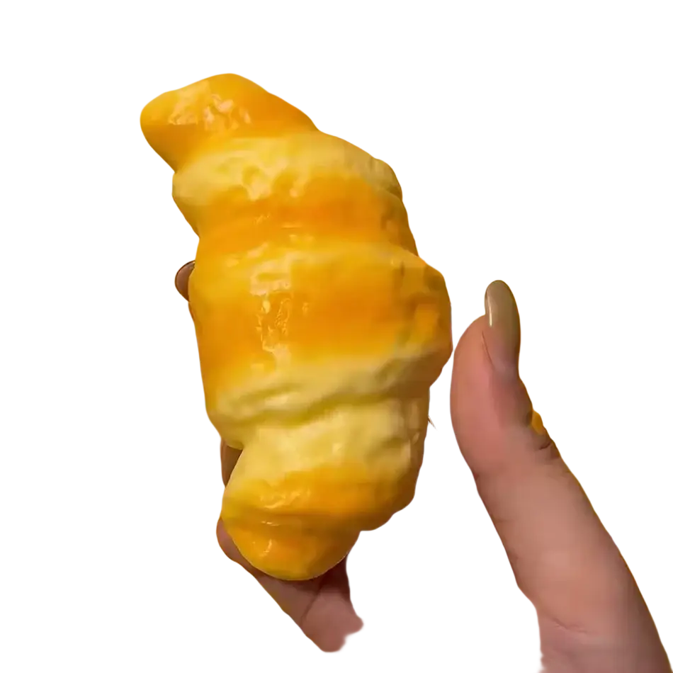 A golden-brown glossy croissant squeeze toy stress relief bread held in hand as a croissant squeeze toy