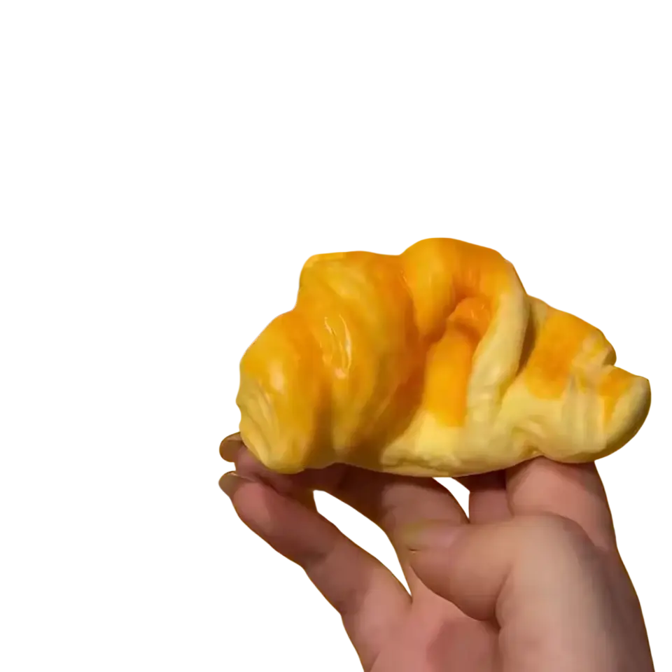 Golden glossy croissant squeeze toy held in hand featuring a flaky texture for stress relief and fun squeezing