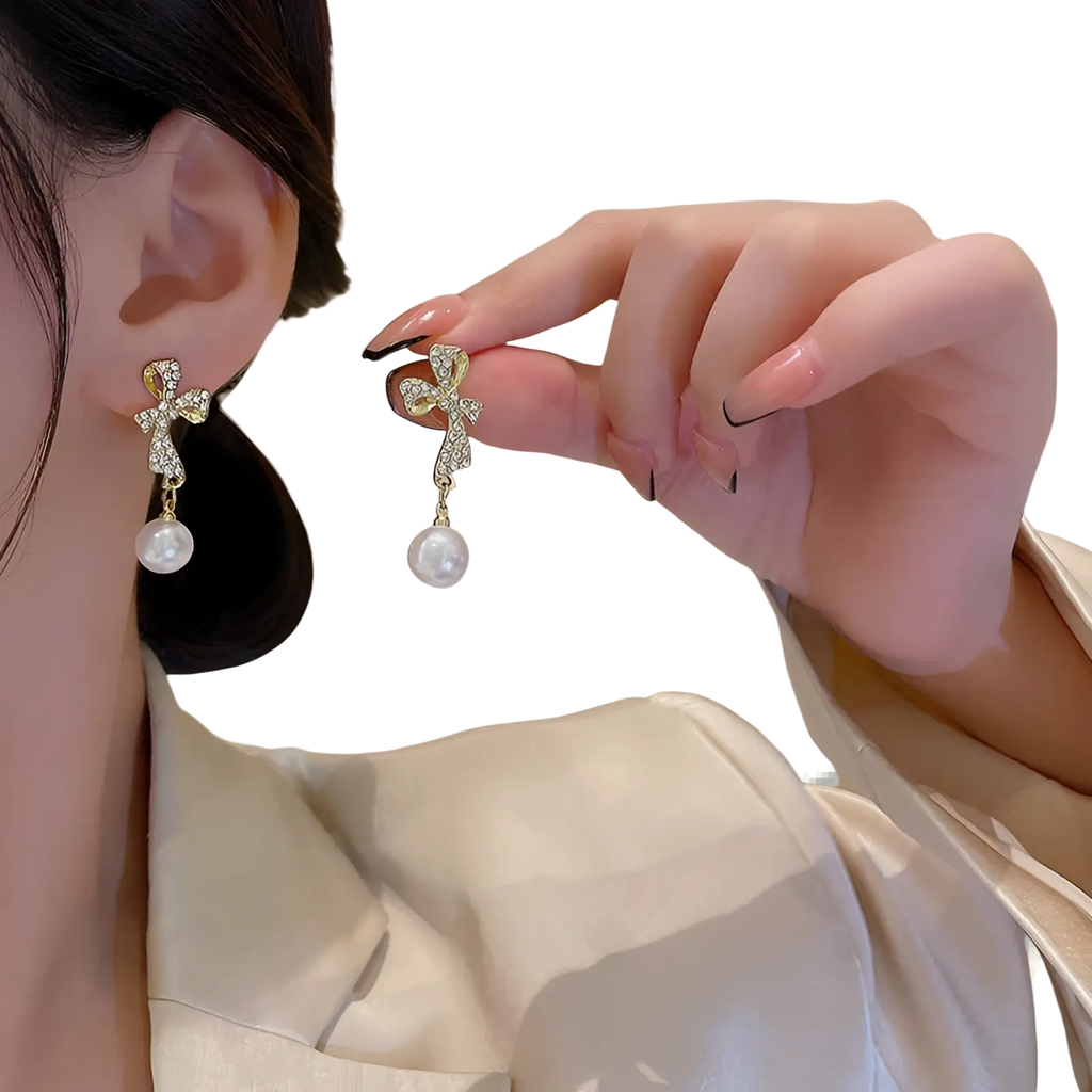 Gold-toned crystal bow and pearl dangle earrings featuring a cross shape with sparkling crystals and white pearls