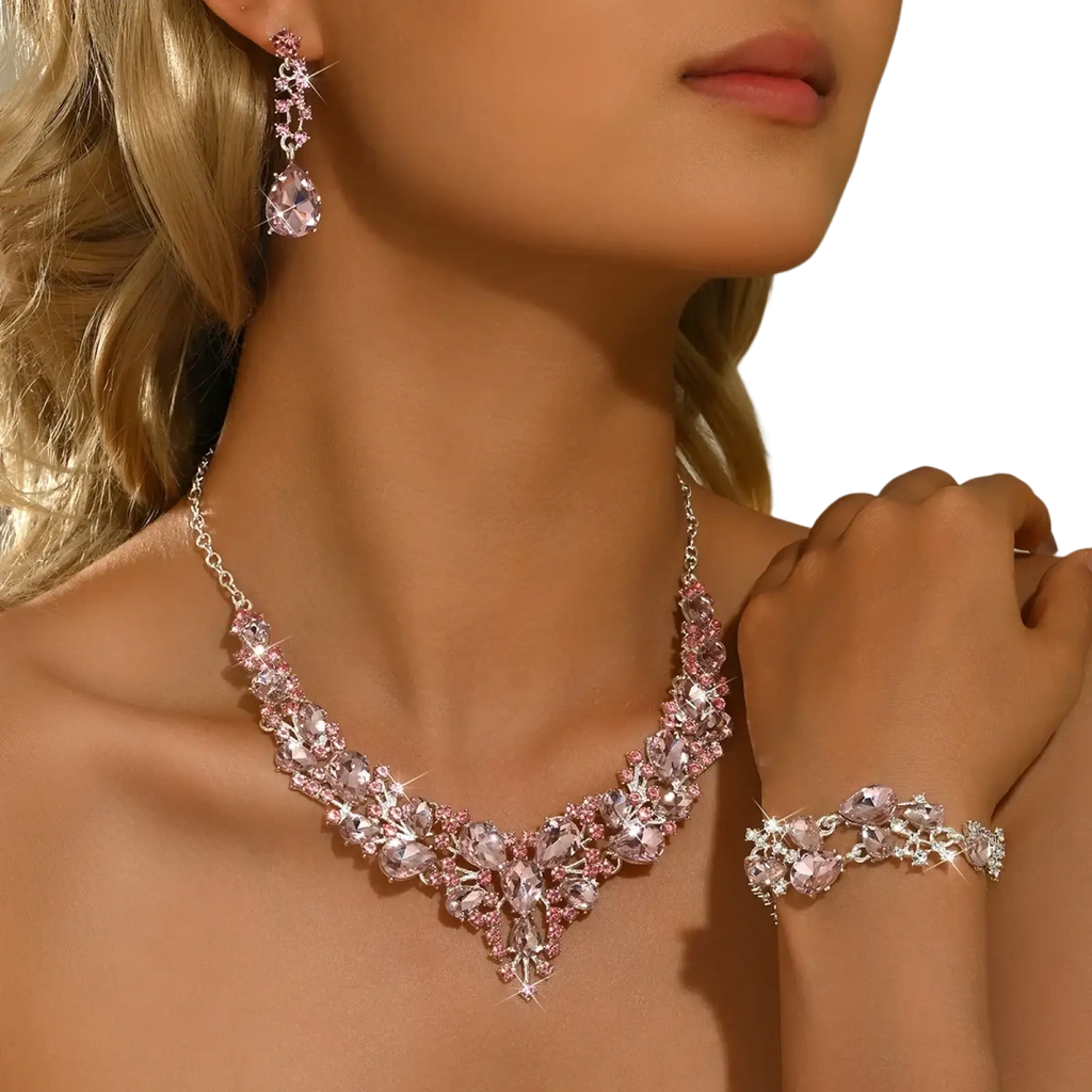A sparkling pink and silver crystal bridal jewelry set with v-neck necklace, matching earrings, and delicate bracelet