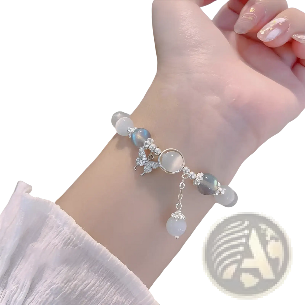 A delicate silver-toned crystal butterfly cat’s eye bead bracelet with translucent white and soft blue beads and a pearl drop