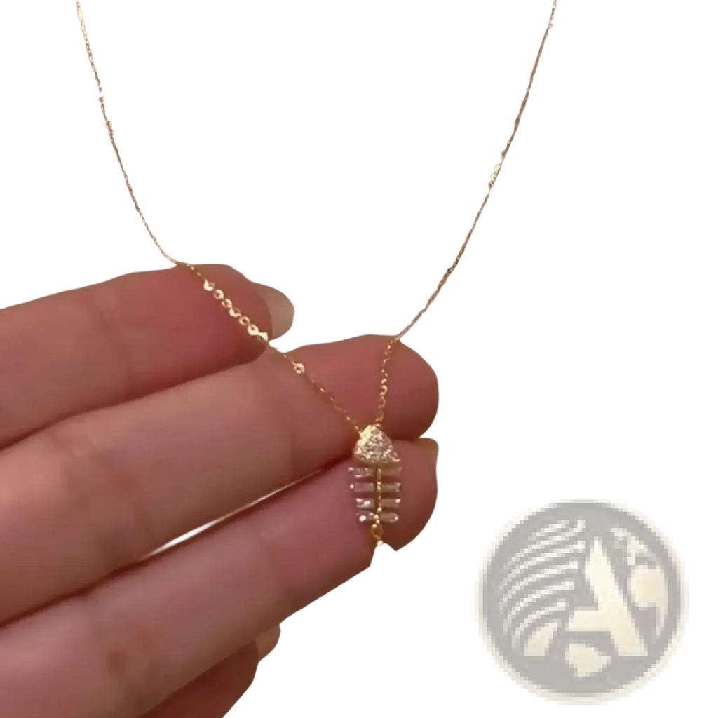 A delicate gold chain necklace with a small crystal-adorned fishbone pendant in clear crystals