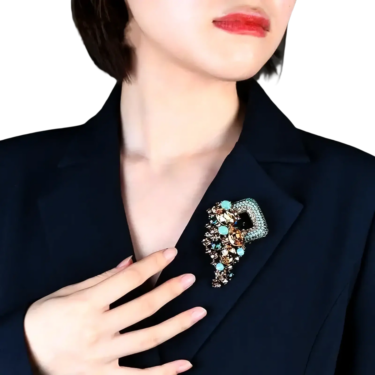 A sparkling turquoise and gold crystal flower brooch pin shaped like a stylized letter b on a navy blazer lapel