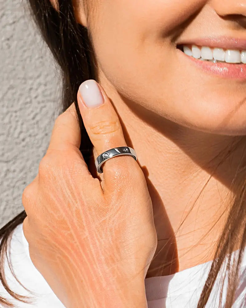 A sleek silver magnetic crystal therapy ring in stainless steel with two embedded diamonds on a woman’s finger