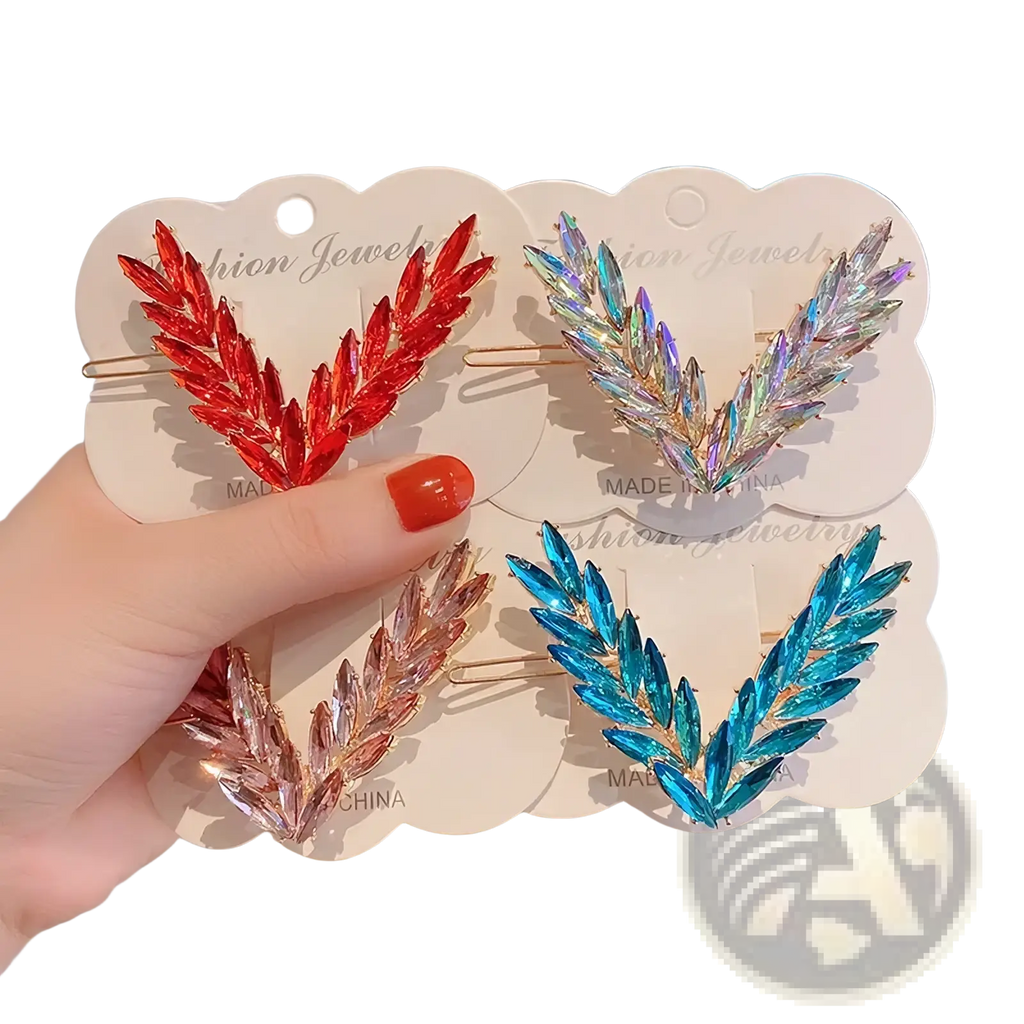 A hand holds four crystal v shape hair clips with sparkling leaf designs in red iridescent rose gold and blue hues