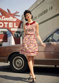 A woman wearing a sleeveless cotton retro cupcake print dress with pockets red collar and matching belt