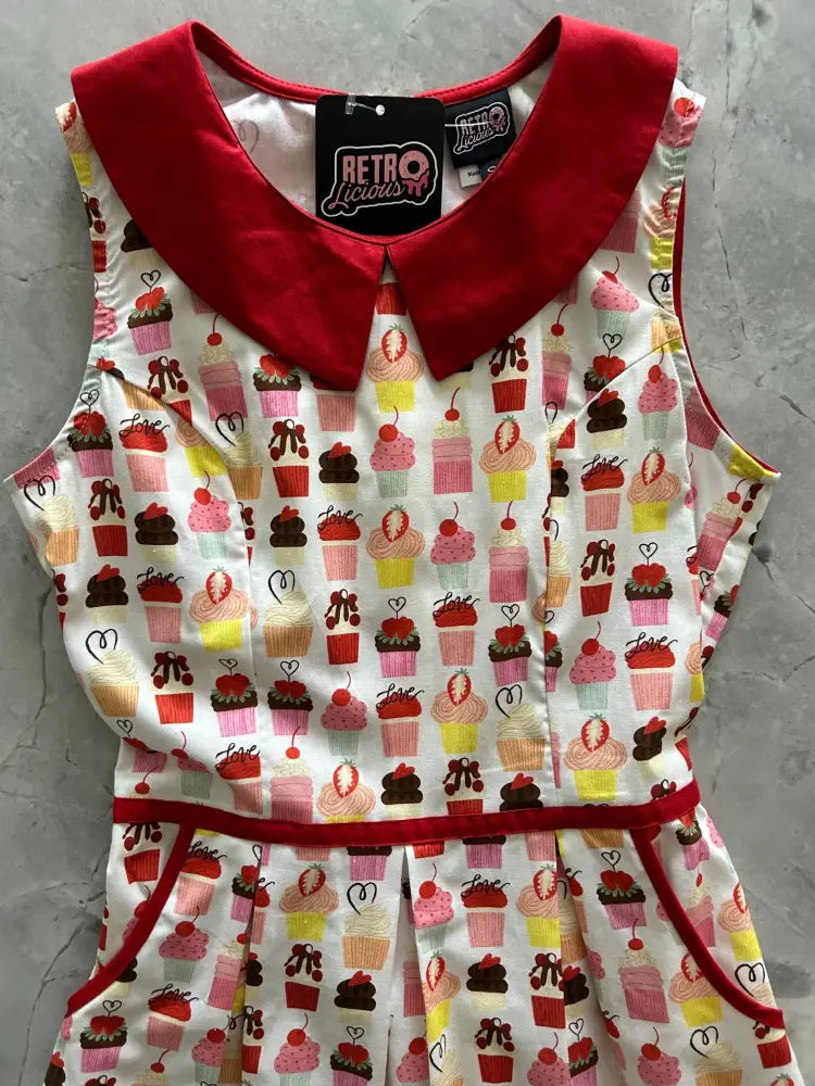 White sleeveless cotton dress with red collar and waistband featuring colorful retro cupcake print and pockets