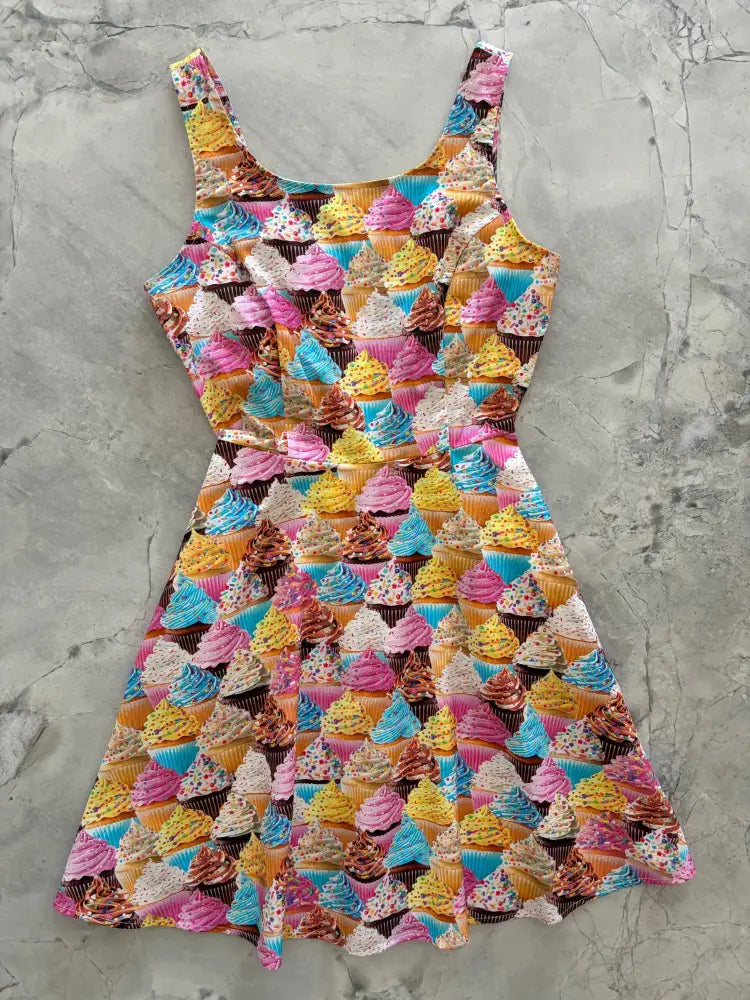 A vibrant sleeveless a-line skater dress with colorful cupcake print and pockets in pink blue yellow and brown