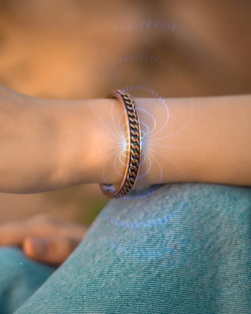 A copper-toned curb chain inlay magnetic therapy cuff bracelet with textured interlocking design worn on a wrist