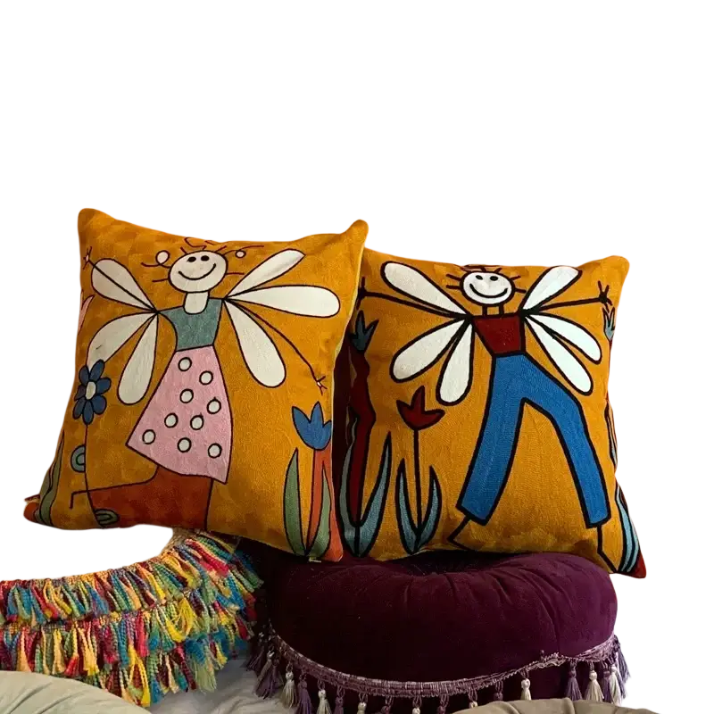 Two mustard-yellow embroidered cushion covers 45x45cm featuring whimsical fairy and human figures with white wings