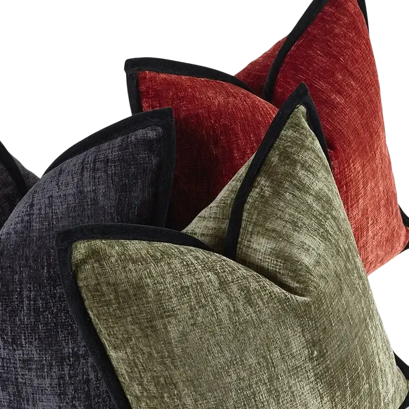 A collection of solid color velvet cushion covers in red, olive green, and charcoal gray with black trim pillow covers