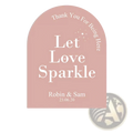 A soft pink arched wedding sticker with white let love sparkle text and personalized names and date for guests