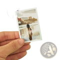 A hand holds a custom couple photo print with white border featuring a man and child walking on a beach