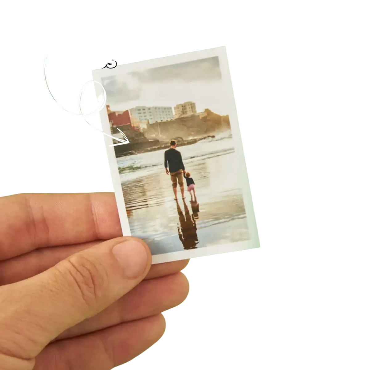 A hand holds a custom couple photo print with white border featuring a man and child walking on a beach