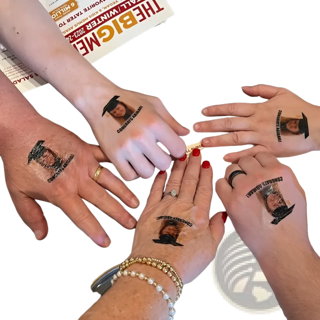 Hands with custom temporary black graduation cap tattoos featuring a constance bennett portrait for party favors