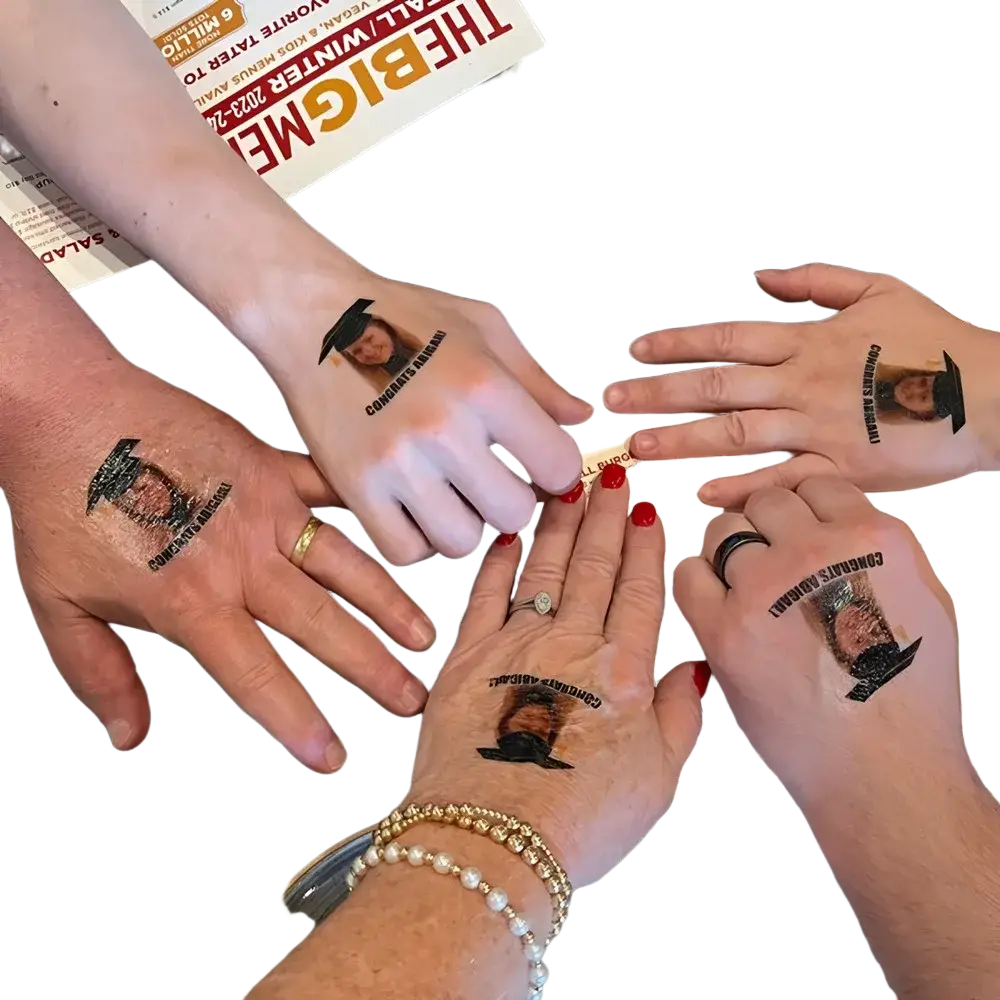 Hands with custom temporary black graduation cap tattoos featuring a constance bennett portrait for party favors