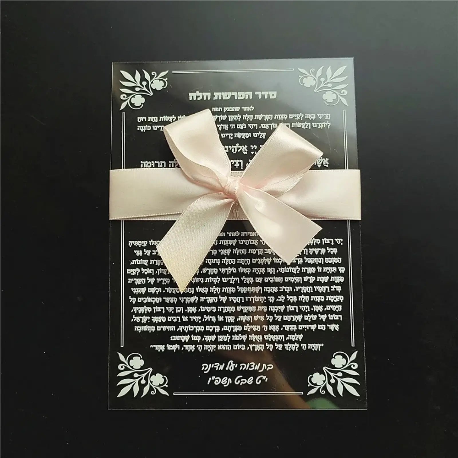 A custom Hebrew acrylic prayer card adorned with floral designs and a delicate cream satin ribbon bow for weddings and bar mitzvahs