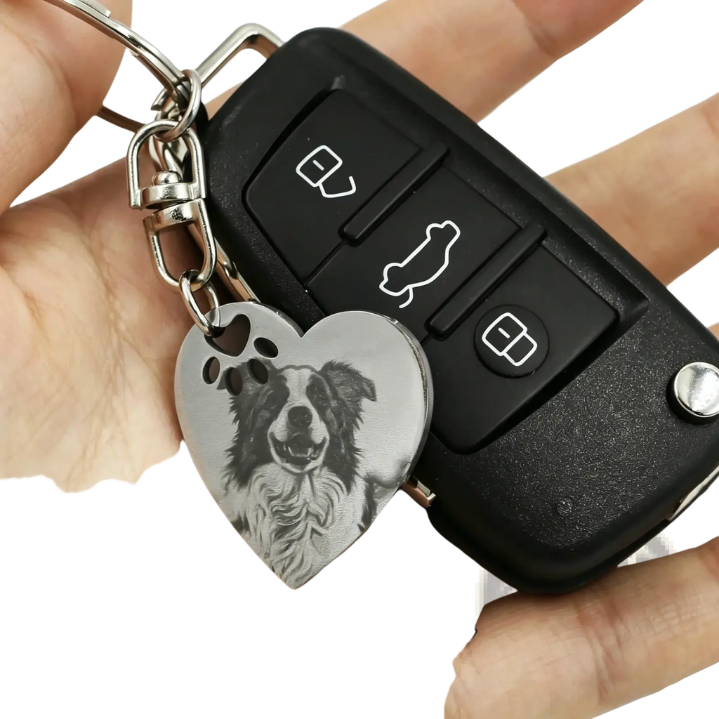 A stainless steel heart keychain engraved with a detailed border collie portrait and paw prints in silver tone