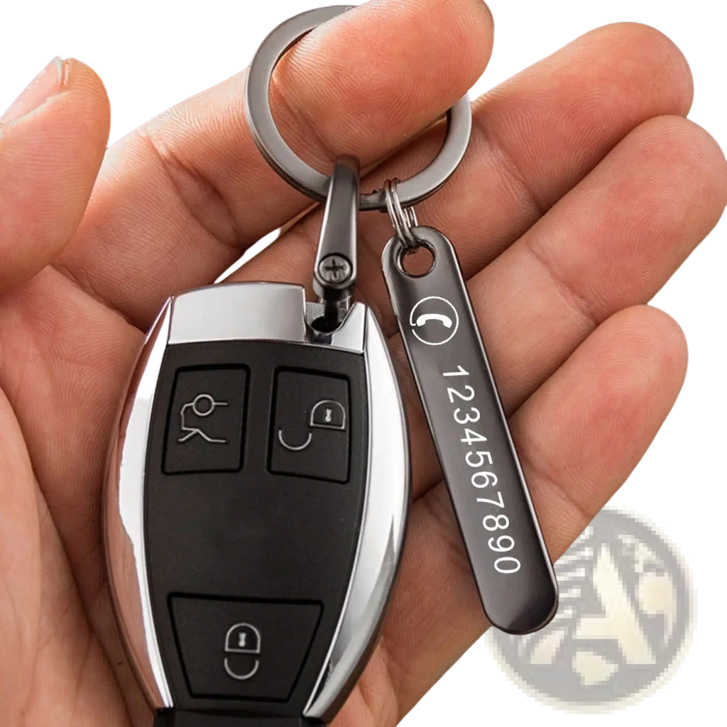 A sleek black and silver car key fob attached to a custom laser engraved metal key ring with phone number tag