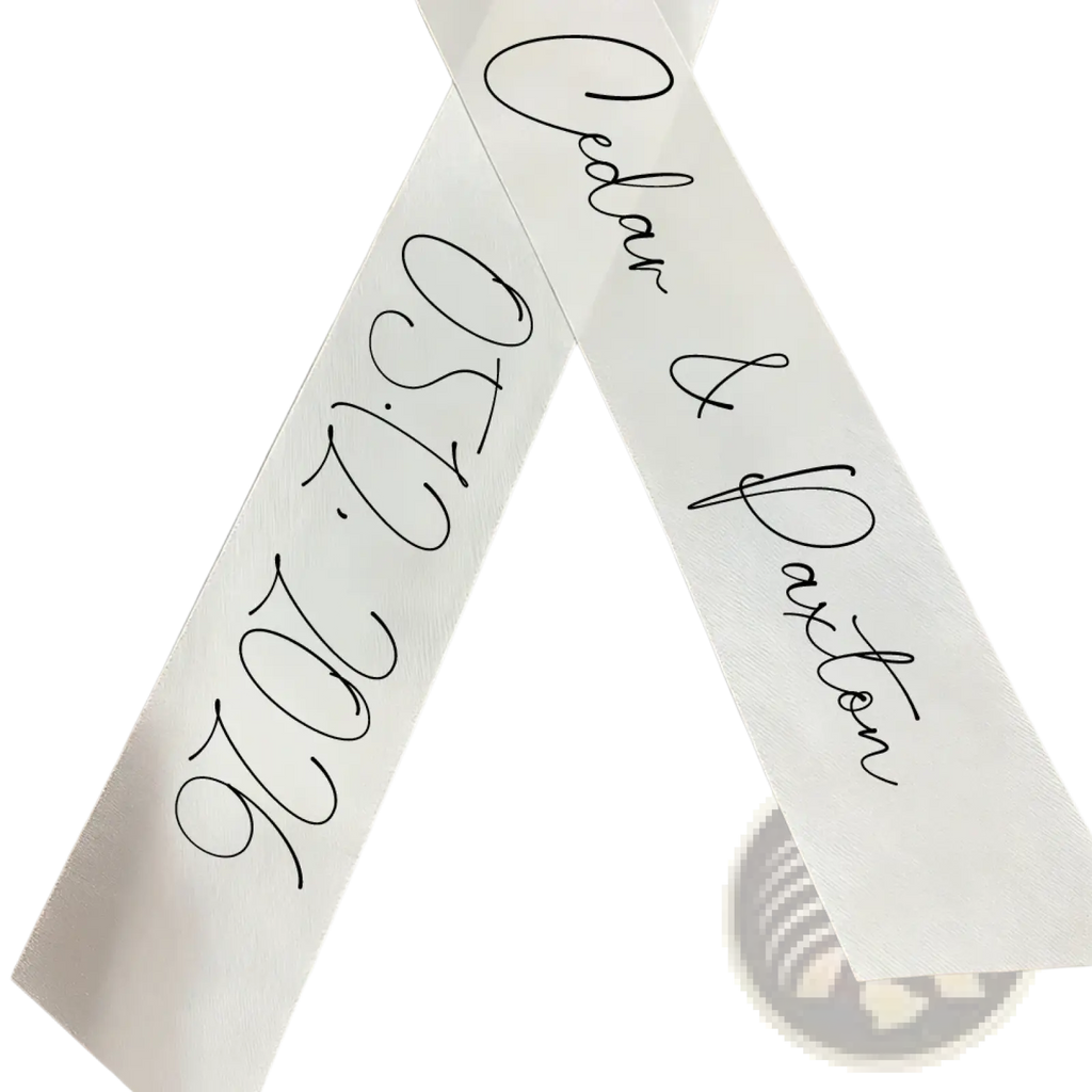 White satin custom wedding bouquet ribbon featuring black cursive script with personal names caden and daxton and date 05122026