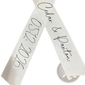 White satin custom wedding bouquet ribbon featuring black cursive script with personal names caden and daxton and date 05122026