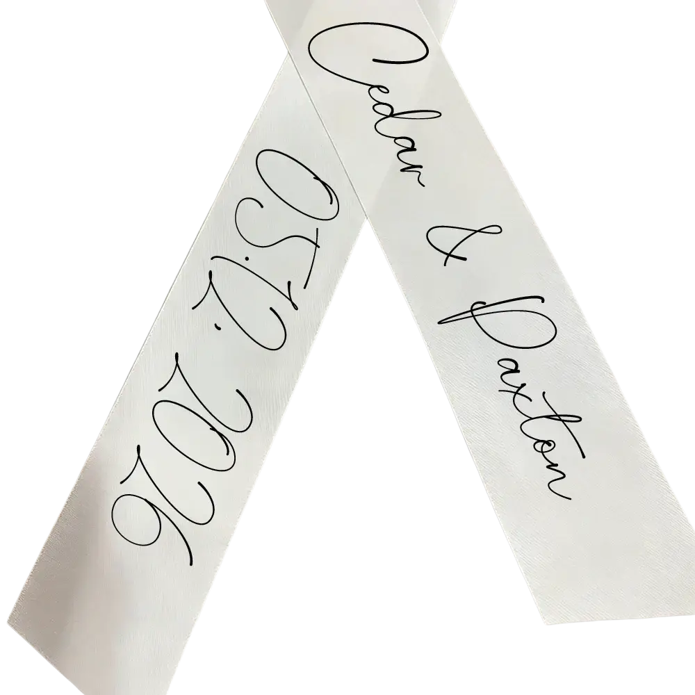 White satin custom wedding bouquet ribbon featuring black cursive script with personal names caden and daxton and date 05122026