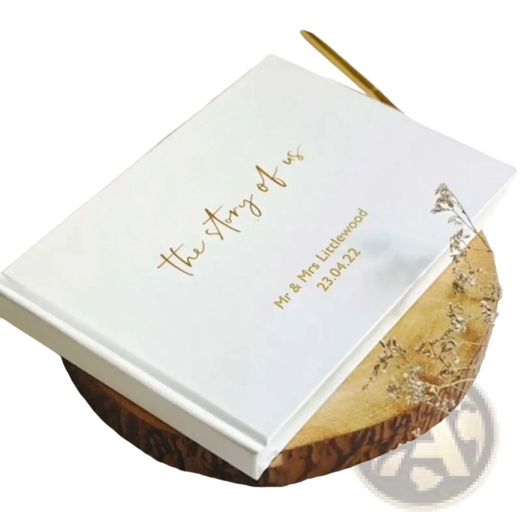 Custom wedding guest book with white hardcover and gold foil lettering resting on wooden slice for keepsake use
