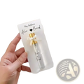 A clear glass custom wedding perfume vial with a gold cap and white ribbon in a personalized gift card