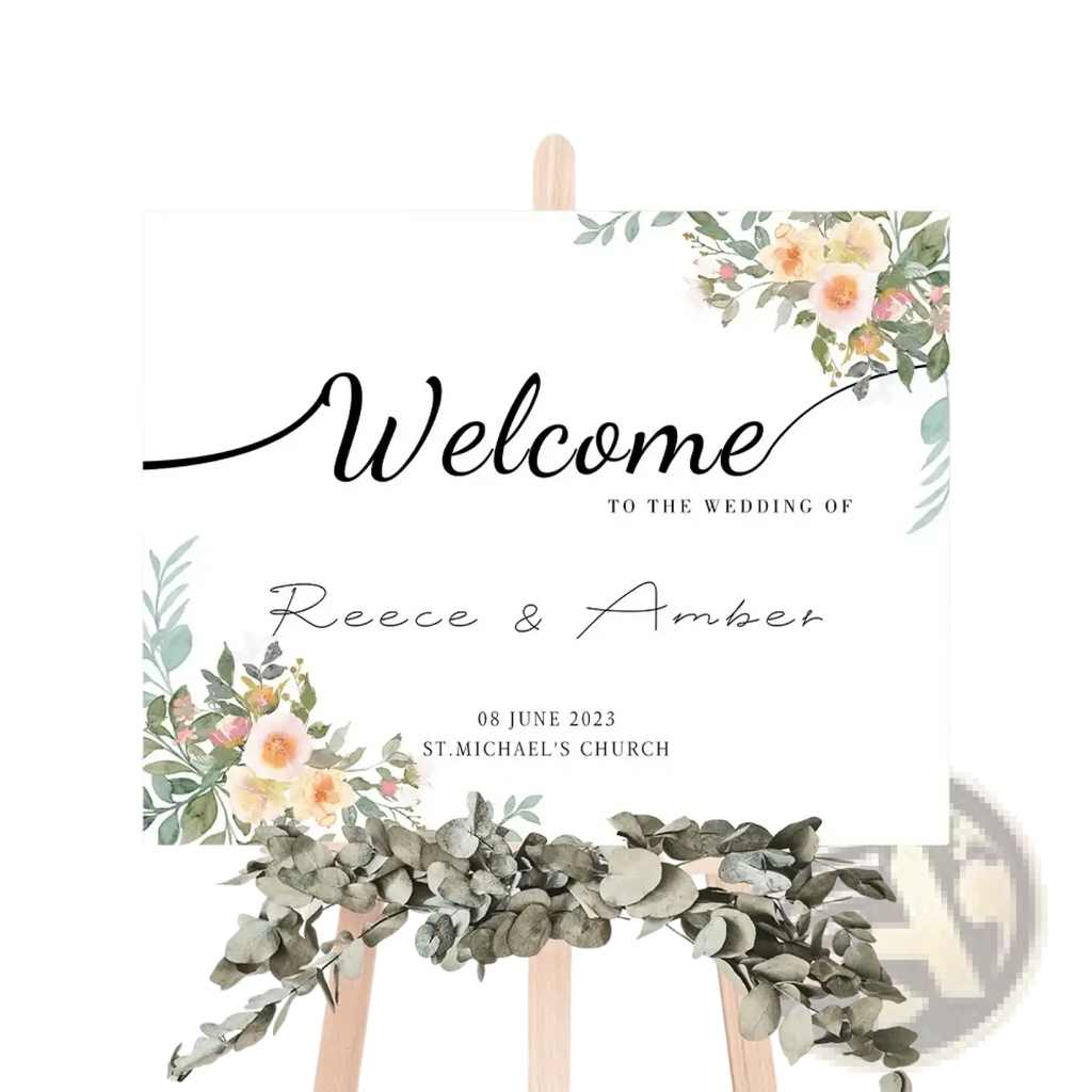 A white custom wedding welcome sign with black cursive lettering and peach pink floral watercolor accents for decor